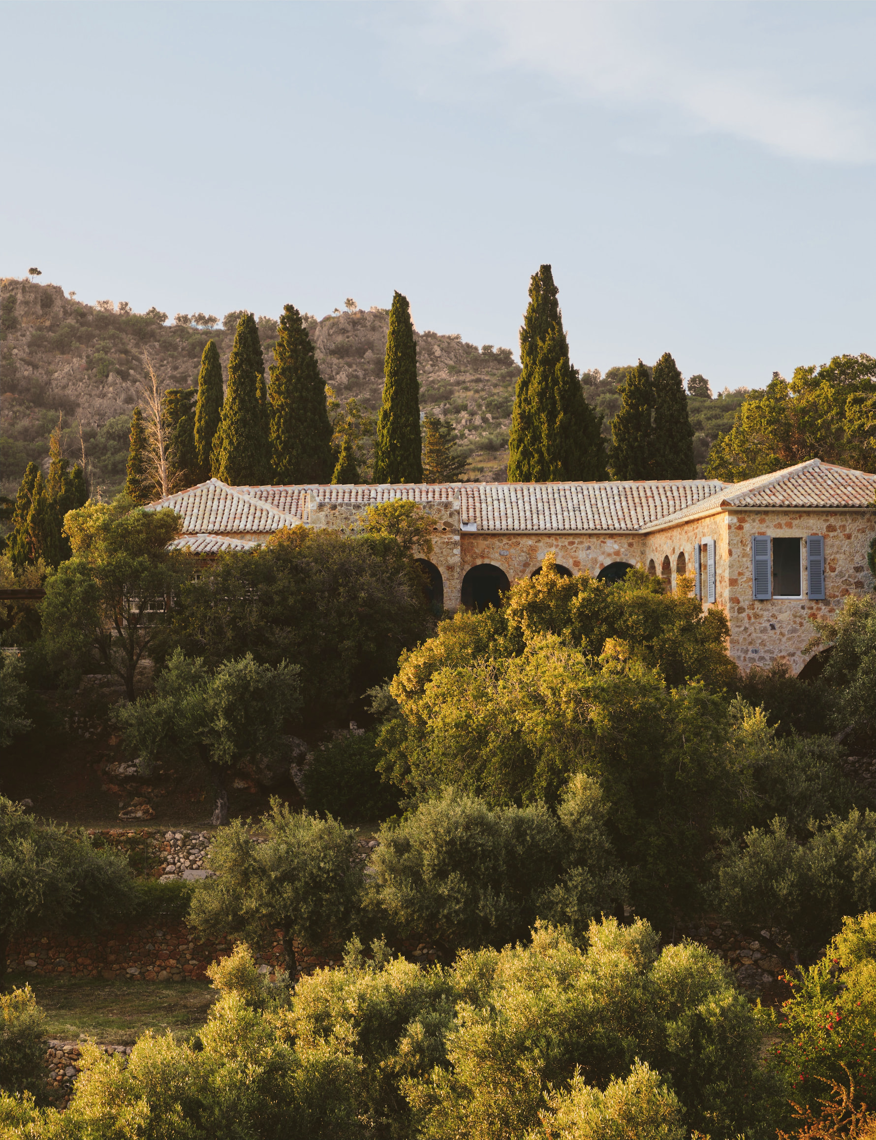 Kardamyli by Guillaume Alan — stone house with tiled roofs and arched loggia among cypresses and olive trees, residence in the Peloponnese, Greece